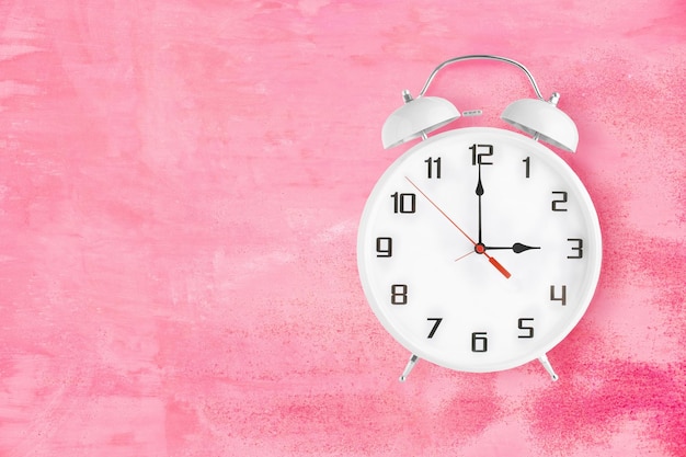 Alarm clock with twin bells and ringer showing 3 o'clock on pink background