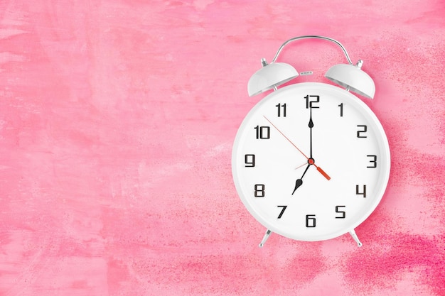 Alarm clock with twin bells and ringer showing seven oclock on pink background