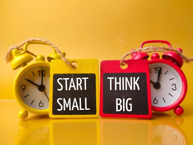 Будильник и деревянная доска с текстом START SMALL THINK BIG на желтом фоне