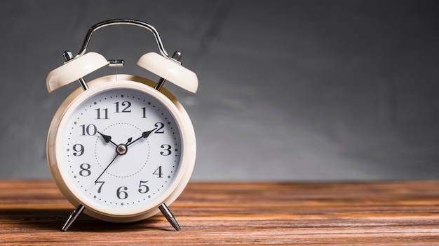 Alarm clock on wooden desk against gray background