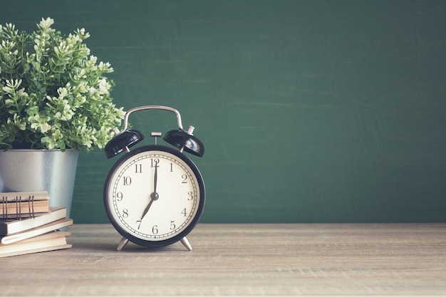 Alarm clock on wooden table on blackboard background in classroom