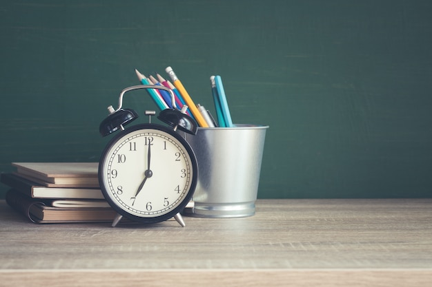 Alarm clock on wooden table on blackboard background in classroom