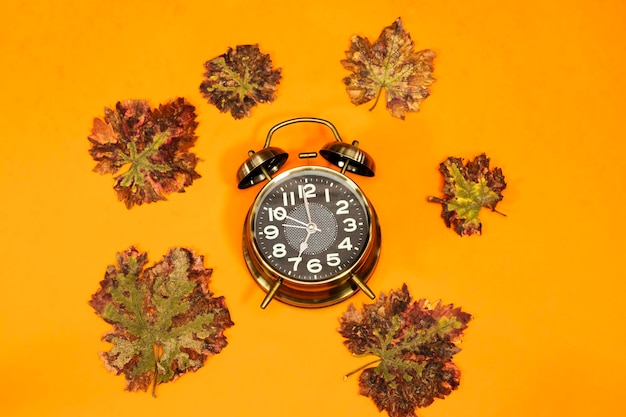 알람 시계는 7 시계와 오렌지색 배경에 고립 된 가을 잎을 보여줍니다.