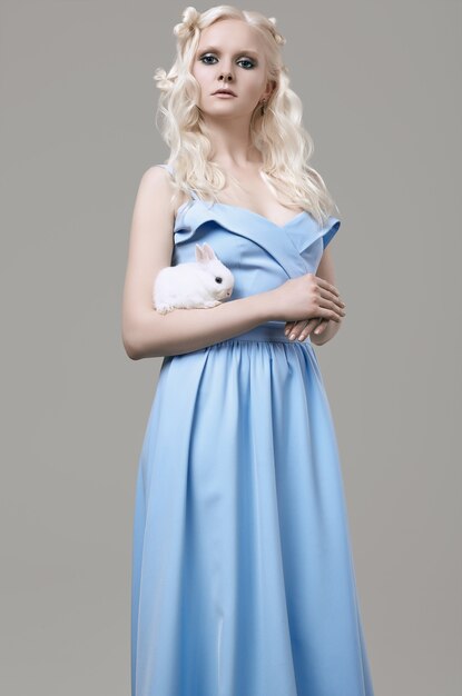 Albino blond girl in elegant dress posing with cute little rabbit