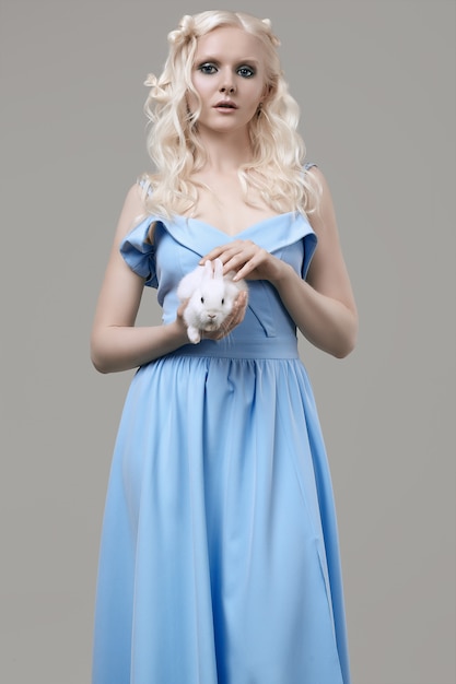 Albino blond girl in elegant dress posing with cute little rabbit