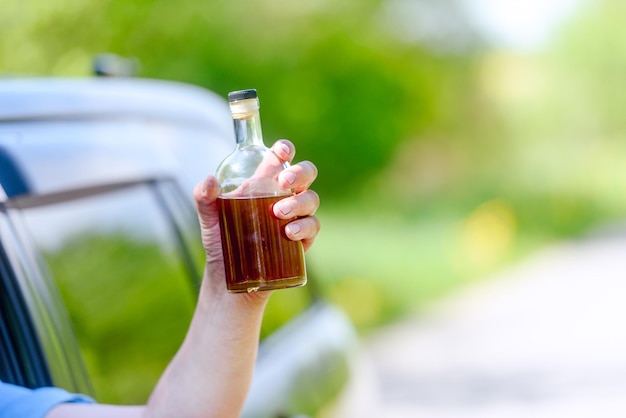 Alcohol bottle car and concept of drunk driving the person holds in hand a bottle with alcoholic drink driving the car Tonted