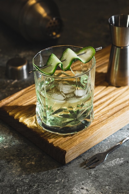 Alcohol cocktail with cucumber in whiskey glass with ice cubes Summer spirit drink and shaker