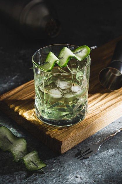 Alcohol cocktail with cucumber in whiskey glass with ice cubes Summer spirit drink and shaker