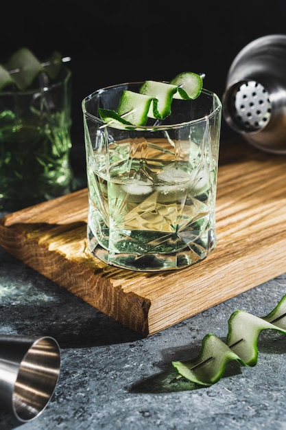 Alcohol cocktail with cucumber in whiskey glass with ice cubes Summer spirit drink and shaker