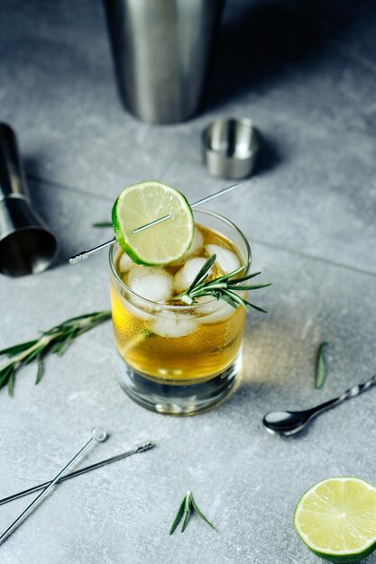 Alcohol cocktail with lime slice rosemary ice and cocktail shaker on black background Party time