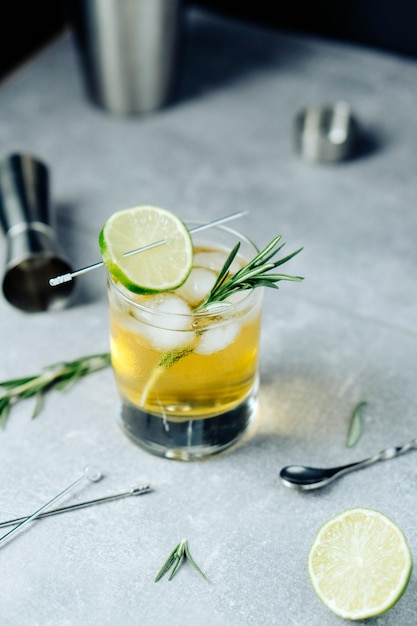 Alcohol cocktail with lime slice rosemary ice and cocktail shaker jigger on black background