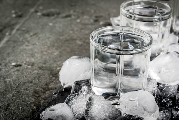 Alcohol and cocktails. Three glasses of vodka on a slate tray, with ice. On a black stone table, 