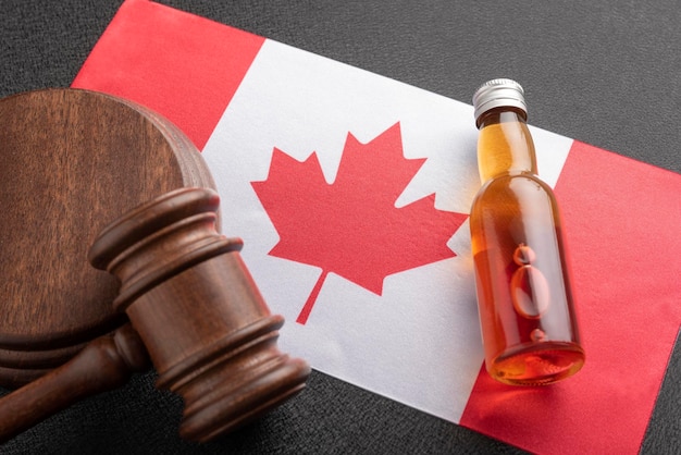 Alcohol and crimes concept Bottle of alcohol and wooden gavel as symbol of law and flag of Canada