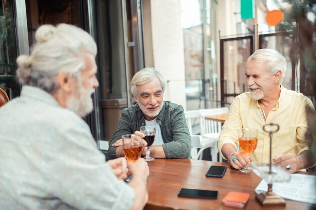 Alcohol drinken en praten. Bebaarde grijsharige mannen die 's avonds alcohol drinken en praten