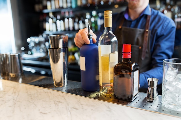 alcohol drinks, people and luxury concept - barman with shaker, bottles and jigger preparing cocktail at bar