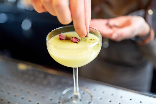 アルコール飲料、人々、豪華なコンセプト – バーでドライフラワーでグラスにカクテルを飾るバーテンダーの手