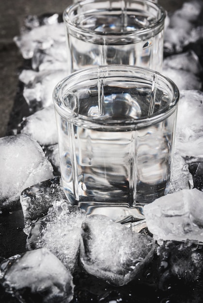 Foto alcohol en cocktails. drie glazen wodka op een leiblad, met ijs. op een zwarte stenen tafel,