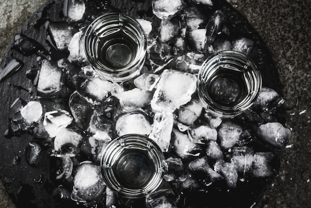 Alcohol en cocktails. Drie glazen wodka op een leien dienblad, met ijs. Op een zwarte stenen tafelblad weergave