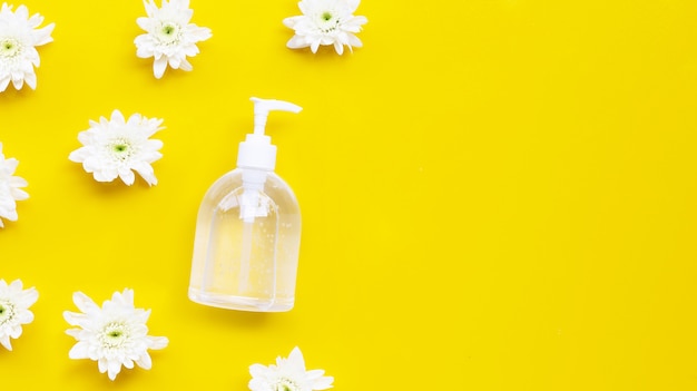 Gel disinfettante per mani alcolico in bottiglia pompa con crisantemo bianco su sfondo giallo.