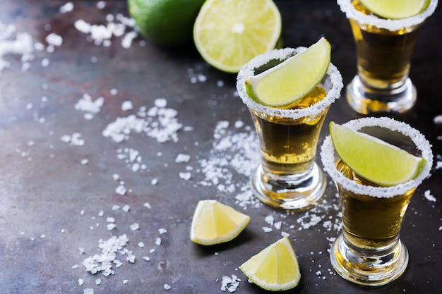 Alcohol junk food party holidays concept Golden mexican tequila shot on a grunge black table with salt and lime Copy space background