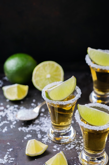 Alcohol junk food party holidays concept Golden mexican tequila shot on a grunge black table with salt and lime Copy space background