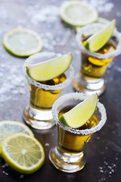 Alcohol junk food party holidays concept Golden mexican tequila shot on a grunge black table with salt and lime