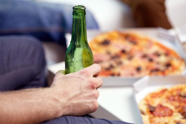 Foto concetto di alcol e persone - uomo con bottiglia di birra e pizza a casa