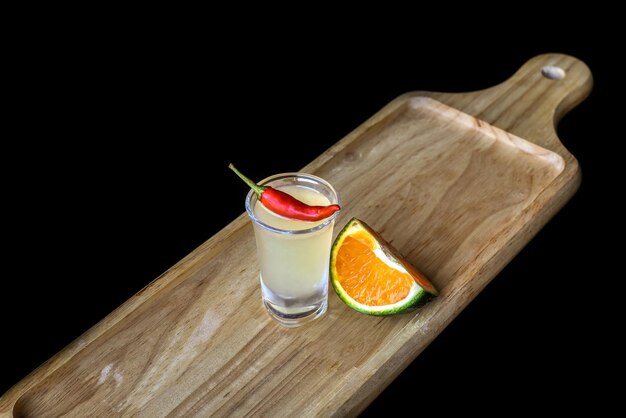 Alcohol shot made of orange juice and chili on wooden board with with copy space