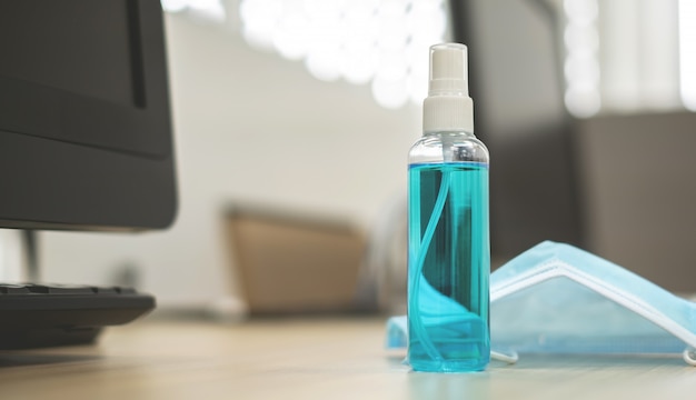 Alcohol spray bottle and mask on a brown wooden table.