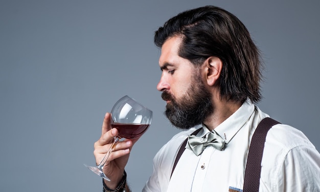 Foto l'uso di alcol è abuso di vita bello hipster bere vino bicchiere sommelier degustazione alcol uomo barbuto in bretelle bere vino rosso brutale ragazzo barista in papillon elegante barman maschio copia spazio