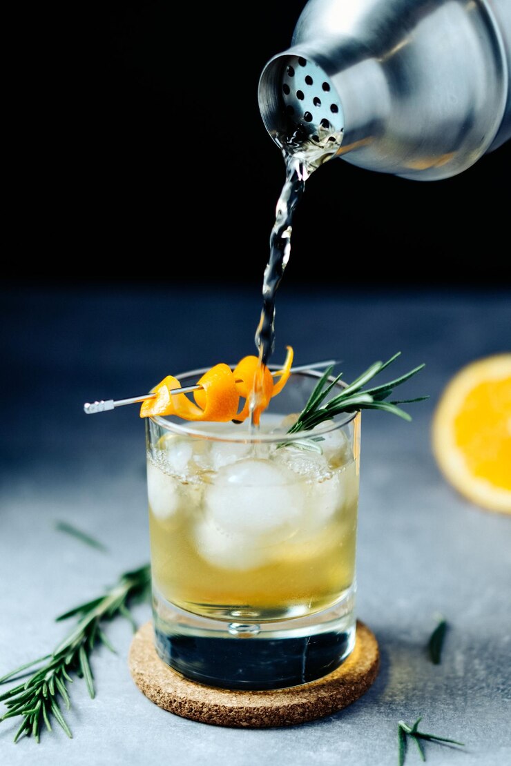 Alcoholcocktail gieten van shaker in glas met sinaasappelschil rozemarijn en ijs op houten bureau