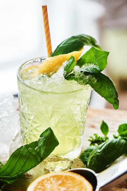 Alcoholic cocktail Basil smash in a glass beaker and a piece of ice on a wooden table