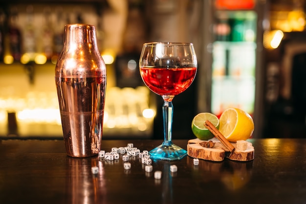 Alcoholic cocktail, shaker and dice on bar counter