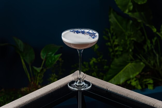 Alcoholic cocktail on a transparent table against a blue background and plants