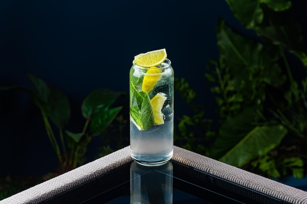 Alcoholic cocktail on a transparent table against a blue background and plants