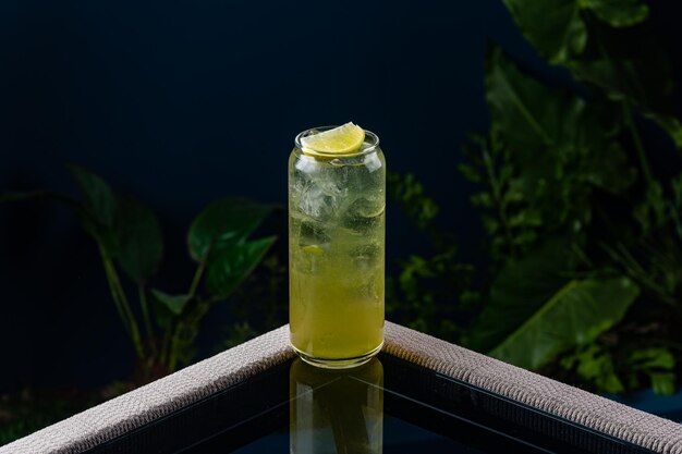 Alcoholic cocktail on a transparent table against a blue background and plants