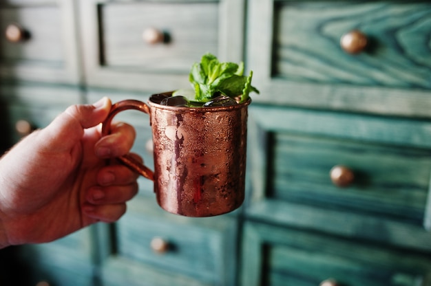 Alcoholic cocktail with ice, mint and lime in bronze cup at hand of barman