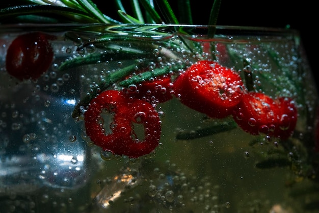Foto cocktail alcolico con ghiaccio e rosmarino e pepperoni su uno sfondo nero macro