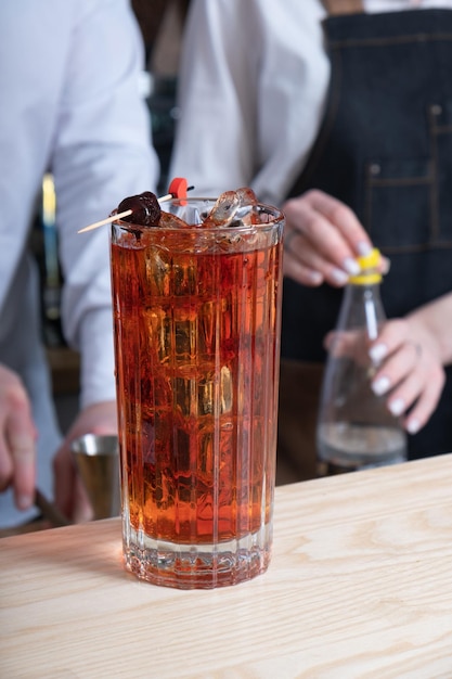 Alcoholic cocktails with ice in glasses on the bar table with bartenedrs in the background