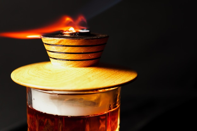 Alcoholic drink A cocktail with whiskey or cognac with fire and smoke closeup dark black background