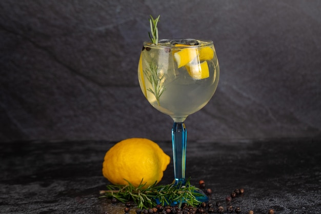 Alcoholic drink gin and tonic cocktail with lemon rosemary pepper and ice on concrete background space for text