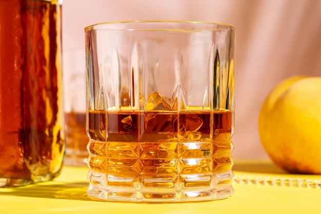 Alcoholic drink in a glass with a peach on a bright background.