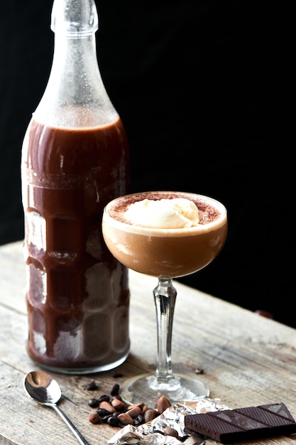 Alcoholische cocktail ice scream russian wordt geserveerd in een glazen fles en drinkbeker op houten tafel op zwarte achtergrond
