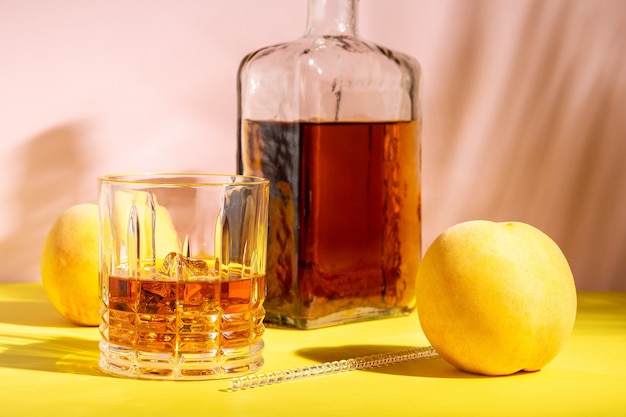 Alcoholische drank in een glas met een perzik op een lichte muur.