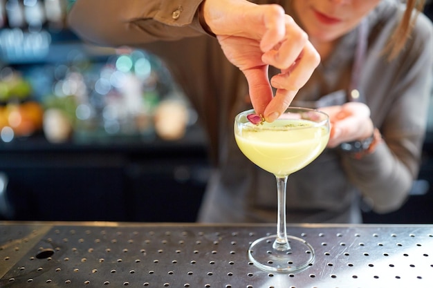 alcoholische dranken, mensen en luxe concept - vrouwelijke barman die cocktail in glas versiert met gedroogde bloemen aan de bar