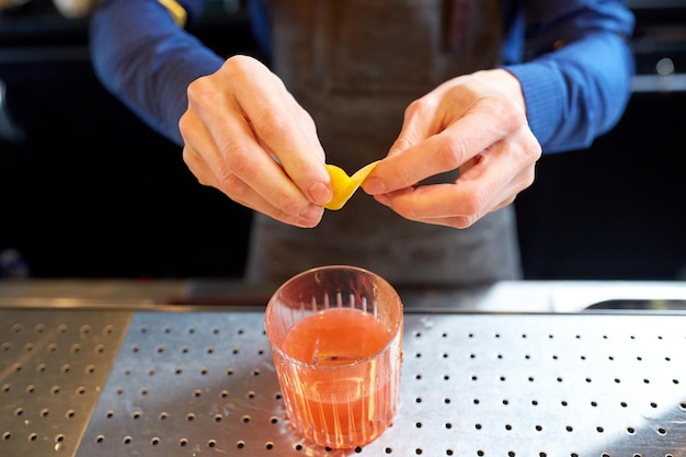 alcoholische dranken, mensen en luxeconcept - barman met glas en citroenschil die cocktail voorbereidt in de bar