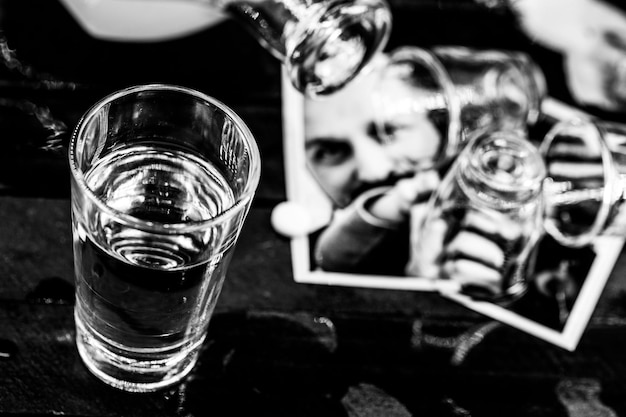 가족의 찢어진 사진 위에 드리워진 술잔이 있는 알코올 중독 테이블 고통과 이혼 컵에 선택적 초점