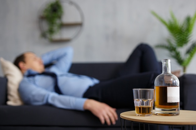 Alcoholisme, stress en bedrijfsconcept - close-up van whiskyfles en glas op tafel en slapende dronken zakenman