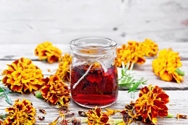 Alcoholtinctuur van goudsbloemen in een glazen pot, verse en gedroogde bloemen met groene bladeren op houten bord achtergrond