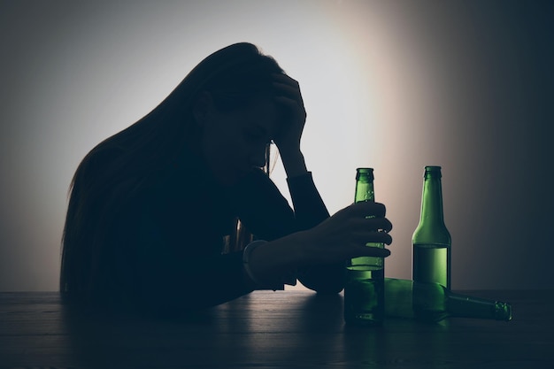 Foto alcoholverslaving silhouet van vrouw met bierflesje aan tafel met achtergrondverlichting
